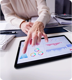 Person pointing at a tablet displaying various graphs and charts, with papers, a keyboard, and a calculator on the desk.