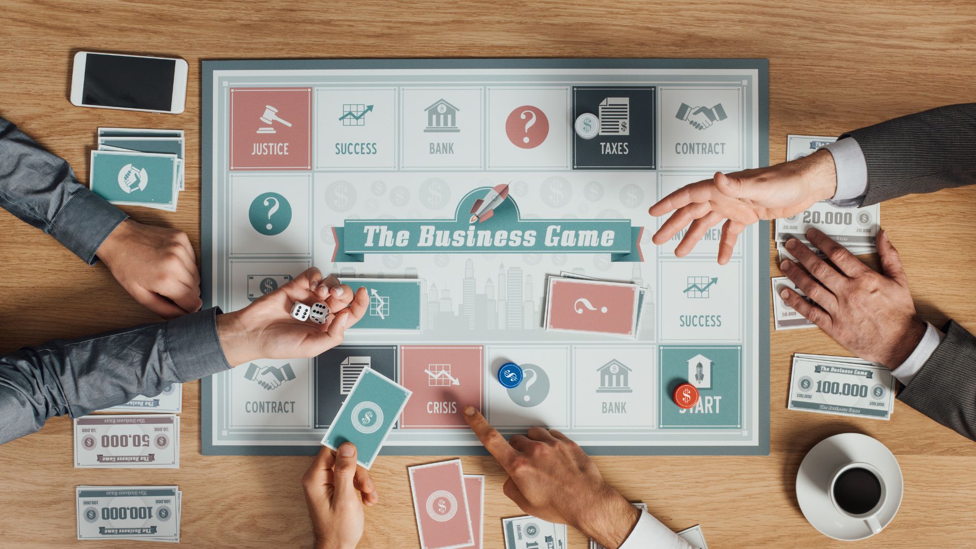 Three people play a board game called "The Business Game" with cards, dice, paper money, and tokens on a table; a cup of coffee sits nearby.