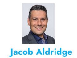 Portrait photo of a man in a suit smiling at the camera, with the name "Jacob Aldridge" written below in blue text—an entrepreneur coach based in Brisbane.